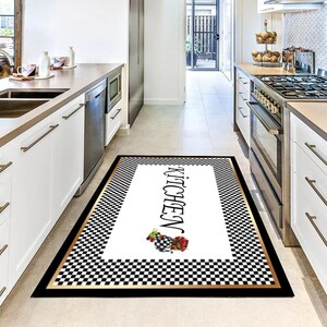 Pode incluir: Um tapete de cozinha retangular com uma borda xadrez em preto e branco e uma moldura dourada. O centro do tapete é branco com a palavra "KITCHEN" em escrita preta e um desenho floral.