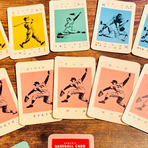 以下が含まれることがあります： 黄色、緑、青、ピンクのイラストが描かれた、ヴィンテージの野球カード。カードには野球選手のアクションが描かれており、日本語のテキストが入っています。「EPOCH'S BASEBALL CARD」と書かれた小さなカードがあります。