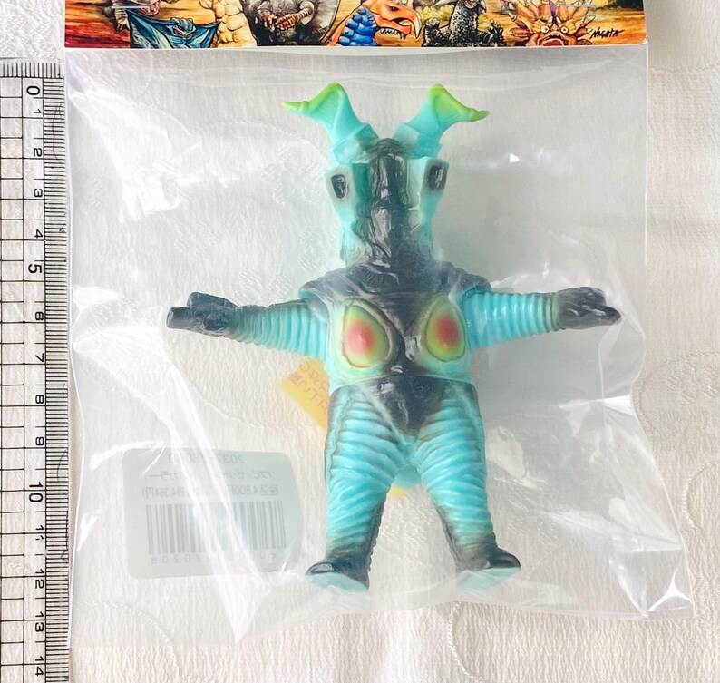 May include: A blue and black monster figurine with green accents, packaged in a clear plastic bag. The figure has outstretched arms and a detailed design, with a light blue torso and legs. The figure is approximately 5 inches tall.