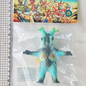 May include: A blue and black monster toy figure in a clear plastic bag. The figure has green horns and a light blue body with black accents. The packaging includes Japanese text and illustrations of other monsters.