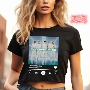 May include: Black crop top featuring a graphic of the Backstreet Boys' album "Millennium 20" with the song title "I Want It That Way." The design includes a music player interface. The text "next day shipping" is also visible.