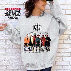 May include: A light gray sweatshirt featuring a graphic of the music group New Edition. The design includes the group's logo, members' names, and album titles. The members are depicted in colorful outfits. The text "NEW EDITION" is prominently displayed.
