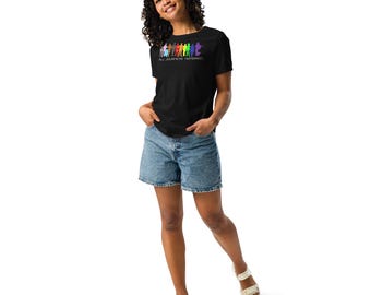 Könnte beinhalten: Schwarzes T-Shirt mit einer Regenbogen-Grafik von Figuren und dem Text "ALL JOURNEYS HONORED". Das Shirt wird mit Jeansshorts und weißen Sandalen getragen.