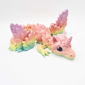 Può includere: Una statuina di unicorno dai colori pastello, con criniera e coda arcobaleno. L'unicorno ha un corpo rosa, un corno a spirale e grandi occhi neri. La statuina è realizzata in materiale stampato in 3D ed è progettata per assomigliare a una creatura mitica.