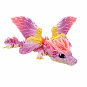 Può includere: Figurina di drago a tema fantasy con grandi ali dettagliate. Il drago presenta una sfumatura di rosa, viola e giallo. La figurina ha una testa, un corpo e zampe dettagliati, con un occhio nero.