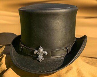 May include: A black leather top hat with a silver fleur-de-lis emblem on a band. The hat has a tall, cylindrical crown and a wide brim. The hat is approximately 7 inches tall.