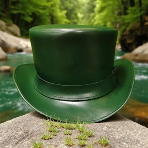 May include: A solid forest green top hat with a smooth, polished finish. The hat features a tall, cylindrical crown and a wide, curved brim. A matching green leather band is stitched around the base of the crown, providing a clean, uniform look.