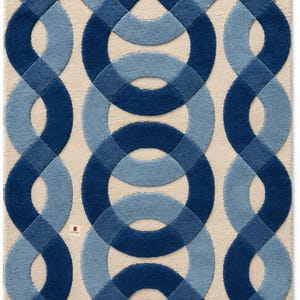 May include: A rectangular area rug featuring a tufted texture with a cream-colored background. The surface displays a repeating geometric pattern of interlocking circles and curved lines in shades of dark navy blue and light sky blue.