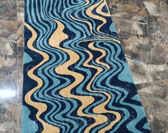 Op de afbeelding: Een rechthoekig vloerkleed met een uniek ontwerp. Het vloerkleed heeft een combinatie van blauwe en bruine golfpatronen, wat een visueel interessant effect creëert. Het ontwerp van het vloerkleed is modern en zou een geweldige aanvulling zijn op elk huis.