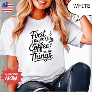 May include: White t-shirt with the text "First I drink the coffee then I do the things" in black. The shirt features a coffee cup graphic and is available now.