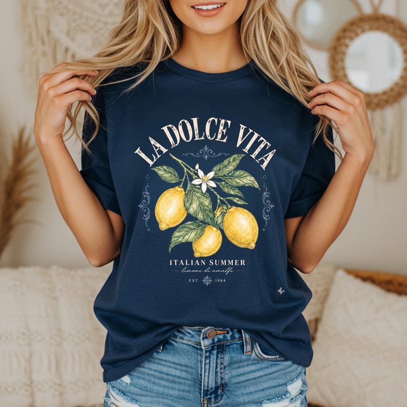 Może przedstawiać: Granatowy t-shirt z grafiką przedstawiającą trzy ż&oacute;łte cytryny na ulistnionej gałązce z białym kwiatem. Napis LA DOLCE VITA, ITALIAN SUMMER, limone di amalfi oraz EST. 1984 znajduje się w białym kolorze na środku przedniej części koszulki.