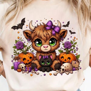 Può includere: T-shirt color crema con grafica a tema Halloween. Il design presenta una mucca delle Highlands dei cartoni animati con un fiocco viola, un gatto nero, zucche, teschi e pipistrelli. L'opera d'arte è colorata e stravagante.