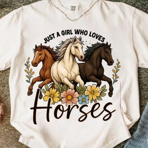 May include: White t-shirt featuring a graphic of three horses in brown, white, and black, surrounded by flowers. The text reads "JUST A GIRL WHO LOVES Horses". The shirt has a crew neck and short sleeves.