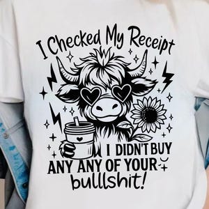 May include: White t-shirt with a black graphic of a cow wearing heart-shaped sunglasses, holding a coffee cup, and a sunflower. The text reads "I Checked My Receipt I Didn't Buy Any of Your Bullshit!"
