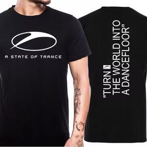 May include: Black t-shirt with a white oval logo and the text "A STATE OF TRANCE". The back of the shirt has the text "TURN THE WORLD INTO A DANCEFLOOR" in white. A short-sleeved crew neck shirt.