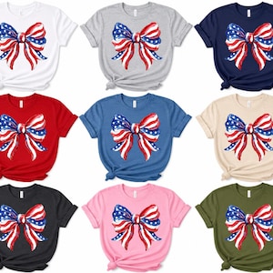 May include: A collection of nine short-sleeved t-shirts in various colors including white, gray, navy, red, blue, beige, black, pink, and olive green. Each shirt features a central graphic of a bow with a red, white, and blue American flag pattern.