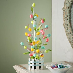 May include: A decorative Easter tree with colorful speckled eggs in shades of yellow, pink, blue, and green. The eggs are attached to white branches with green leaves and curly accents, set in a white picket fence-style pot.