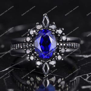 May include: A black engagement ring set with a large oval, deep blue gemstone as the centerpiece. The ring is surrounded by smaller black gemstones and has a matching band. The ring is set against a dark background.