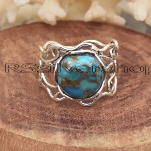 Può includere: Un anello d'argento con una grande pietra turchese rotonda con venature marroni. L'anello ha un design traforato decorativo attorno alla pietra. L'anello è su una superficie di legno. Il testo "RSsilvershop" è visibile.