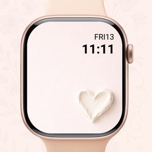 May include: A rose gold smartwatch with a light pink band. The watch face displays the time 11:11 and the date FRI13. A white heart shape is at the bottom of the watch face.