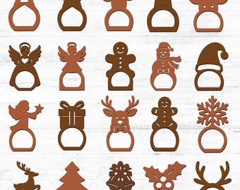 May include: A selection of brown wooden Christmas napkin rings. Designs include a house, star, reindeer, angel, gingerbread man, snowman, gift, Christmas tree, snowflake, holly, and a Santa hat.