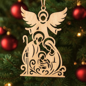 May include: Wooden Christmas ornament depicting the Nativity scene, with an angel at the top. The ornament shows Mary, Joseph, and baby Jesus, with decorative scrollwork at the base. It is suspended from a natural twine string.