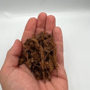 May include: A handful of brown, shredded coconut husk, with a light brown color and a rough texture. The coconut husk is held in an open hand against a white background. The husk appears to be for gardening or pet bedding.