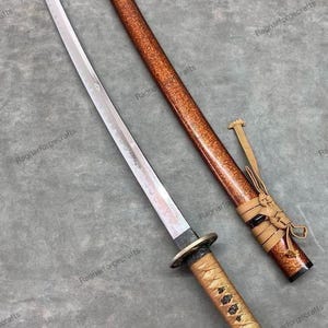 May include: A Japanese katana sword with a polished steel blade and a decorative handle wrapped in tan cord. The scabbard is a speckled brown with a matching cord and knot.