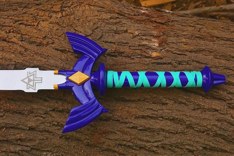 Pu&ograve; includere: Una spada giocattolo con lama argentata decorata da un emblema triangolare nero, una guardia blu scuro con un diamante dorato centrale e un'impugnatura avvolta da un nastro turchese brillante. Il pomolo e la guardia sono in plastica blu lucida.