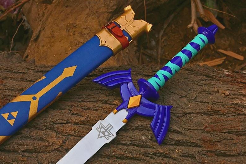 Pu&ograve; includere: Una spada blu e oro con fodero abbinato. La spada presenta una lama argentata con un emblema triangolare, una guardia viola a forma di ali e un'impugnatura avvolta in color ottanio e viola. Il fodero blu presenta dettagli color oro.