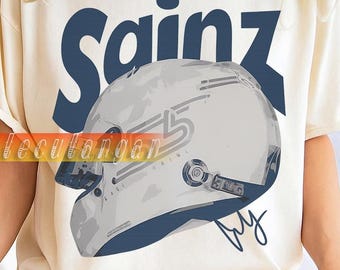 Peut inclure: T-shirt crème avec le nom "Sainz" en bleu marine au-dessus d'un casque de course gris et bleu marine. Le t-shirt a des manches courtes et une coupe décontractée. Une tasse blanche est tenue dans la main de la personne.