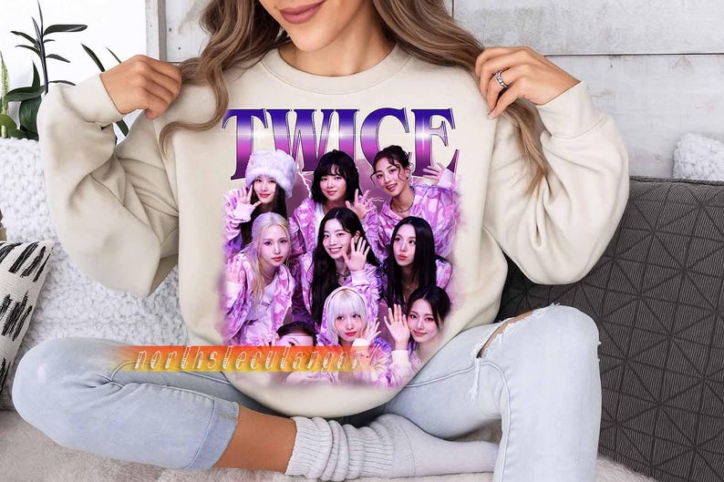May include: Beige sweatshirt with a graphic of the K-pop group TWICE. The graphic shows the word "TWICE" in purple and pink, and images of the group members in pink and purple outfits. The sweatshirt is being worn by a person.