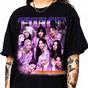May include: Black t-shirt with a graphic of the K-pop group TWICE. The design features the group's name in a purple gradient font and images of the members in pink and purple outfits. The shirt has a crew neck and short sleeves.