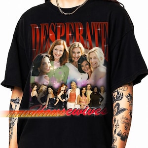 Puede incluir: Camiseta negra con un gráfico del elenco de Desperate Housewives. El diseño incluye la palabra "DESPERATE" en rojo, con letras brillantes sobre un collage de las actrices. Las palabras "northshoreewives" están en la parte inferior.