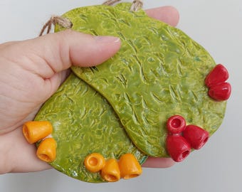 May include: Two flat, oval-shaped ceramic ornaments with a textured, glossy lime green glaze. One ornament features small, bright orange cone-shaped accents, while the other has vibrant red cone-shaped accents. Each piece includes a jute twine loop.