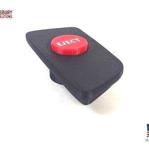 Peut inclure: Un bouton rectangulaire noir avec un bouton circulaire rouge sur le dessus. Le bouton rouge porte le mot "EJECT" en blanc. L'image comprend également le texte "MADE IN USA" et le drapeau américain.