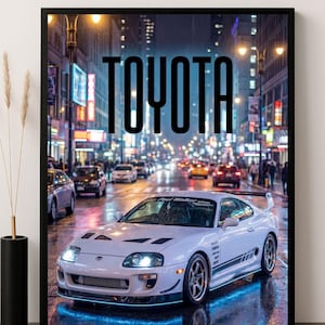 May include: White Toyota Supra sports car poster with the word TOYOTA in large black letters. The car is on a wet city street at night, with headlights on and a spoiler. The background shows city lights.