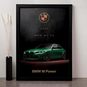 Puede incluir: Impresión enmarcada con un coche BMW M3 CS verde. La impresión tiene un fondo negro con el logotipo de BMW, el año 2023 y el texto "BMW M Power" en dorado. El coche está centrado e iluminado.