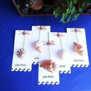 May include: Five white cards with a seashell attached to a silver chain. Each card has a black and white drawing of a ceiling fan and the text "FAN PULL".