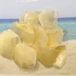 May include: A pile of translucent, pale yellow, seashell-shaped soap bars on a white sandy beach.