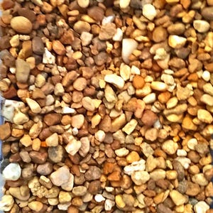 May include: A close-up view of a collection of small, smooth river rocks. The rocks vary in size and shape, with a mix of colors including tan, brown, beige, and white. The texture appears natural and slightly glossy.