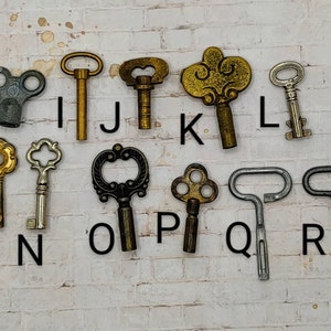 May include: A collection of 10 antique keys with various designs and finishes, including gold, silver, and black. The keys are arranged in rows on a white brick background, labeled with letters from H to R.