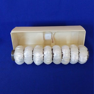 May include: A set of eight clear, textured, cylindrical bracelets displayed in a beige box against a blue background. The bracelets have a ribbed design and are made of a translucent material. The box is open, revealing the bracelets.