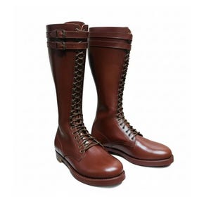 Puede incluir: Un par de botas altas de cuero marrón. Las botas presentan un diseño con cordones, correas con hebillas y una puntera redondeada. Las botas están hechas de cuero liso y pulido y tienen una suela resistente.