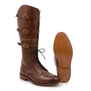 May include: A pair of brown knee-high boots featuring three horizontal straps with brass-toned buckles across the upper shaft, black laces, and a smooth leather finish. The text MorarLeather is visible on the side, with a separate sole view.