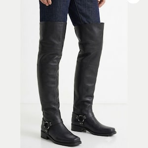 Op de afbeelding: Zwarte overknee laarzen van leer met een vierkante neus, een lage blokhak en een harnasband met een zilverkleurige metalen ring en studs bij de enkel. De laarzen komen tot boven de knie en bevatten een logolabel met de tekst MORAR LEATHER GEAR.