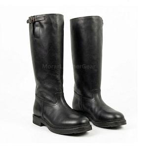 Puede incluir: Un par de botas de montar de cuero negro. Las botas son altas, con una hebilla en la parte superior y una suela resistente. Las botas se muestran sobre un fondo blanco. La marca "Morar Leather Gear" es visible.