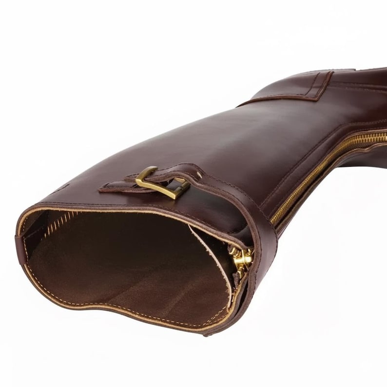 May include: A close-up of a brown leather riding boot. The boot features a gold zipper, buckle, and strap details. The interior of the boot is visible, showing the brown lining and stitching. The boot is set against a white background.