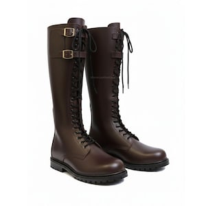 May include: A pair of tall, brown leather boots with black laces and buckles. The boots have a knee-high design with a rounded toe and a sturdy sole. The boots are designed for riding or equestrian activities.