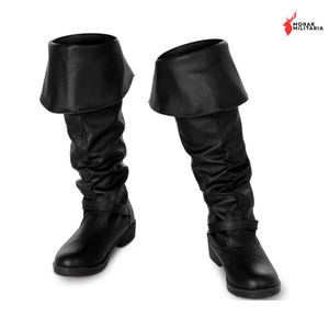 Puede incluir: Un par de botas negras hasta la rodilla con un borde ancho y doblado en la parte superior, un diseño de caña holgada y una tira horizontal delgada en la zona del tobillo. Las botas tienen una punta redondeada y un acabado mate y liso.